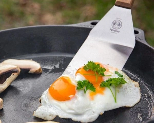 Bucati de ciuperci si ochi de ou in tigaie de fonta si spatula din inox cu maner de lemn